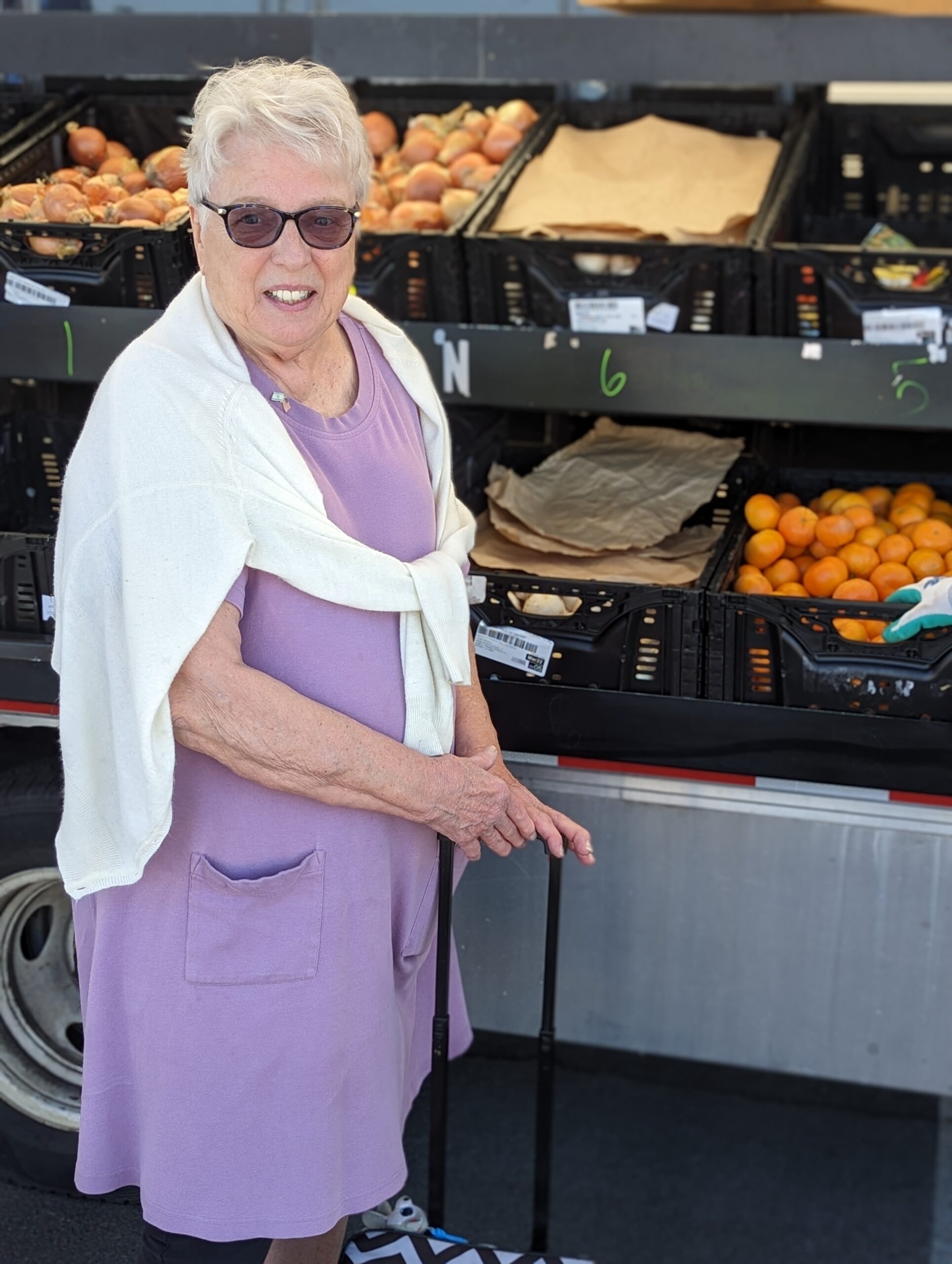 Ann stands in front of the Produce on Wheels truck, with fresh produce visible in the background.