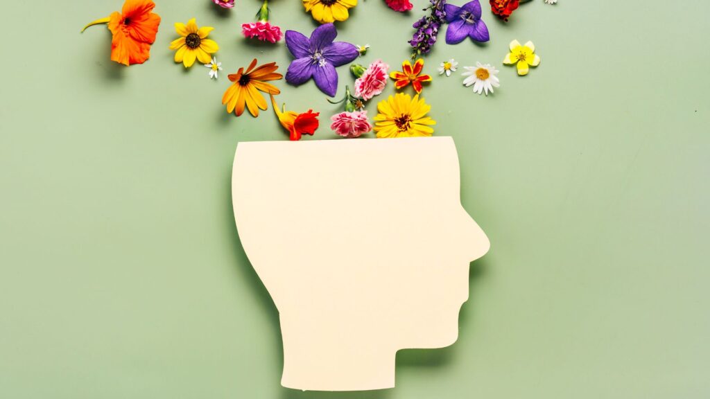 Paper cut human head symbol and flowers on green background symbolizing positive mental health.